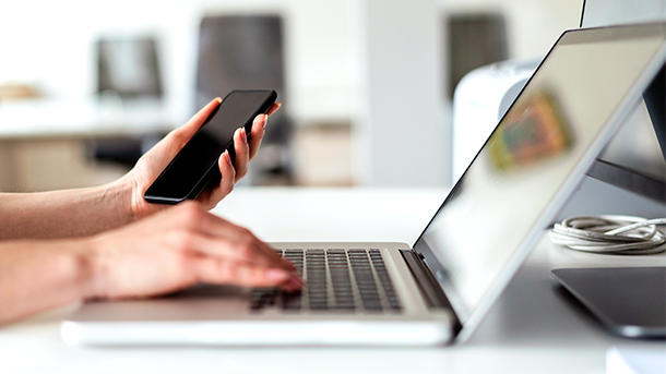 Close up of hands holding a mobile phone and using a laptop